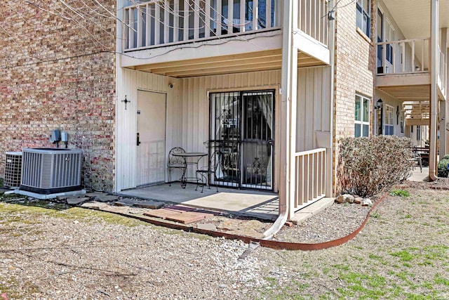 property entrance featuring brick siding, central AC, and a balcony