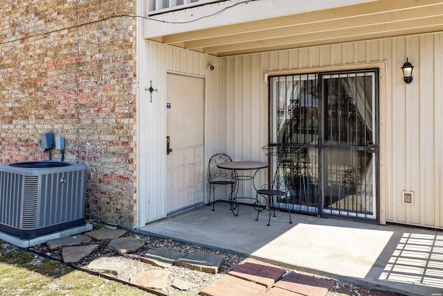 doorway to property featuring a patio area, central AC unit, and brick siding