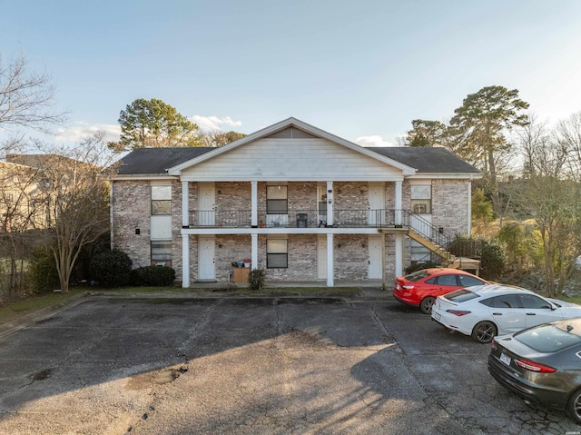 view of front of home with uncovered parking, stone siding, stairway, and a balcony