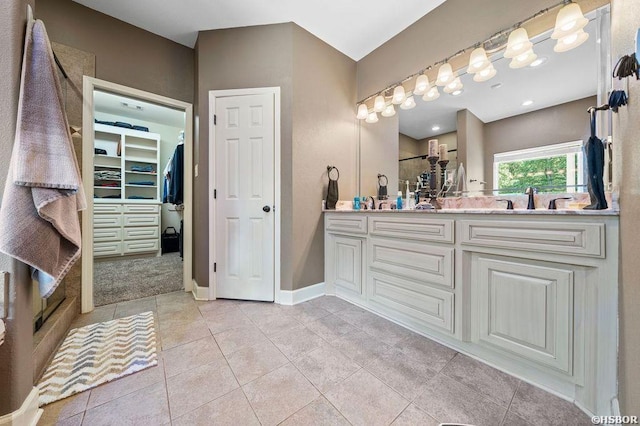 full bath featuring double vanity, a stall shower, tile patterned floors, a walk in closet, and a sink