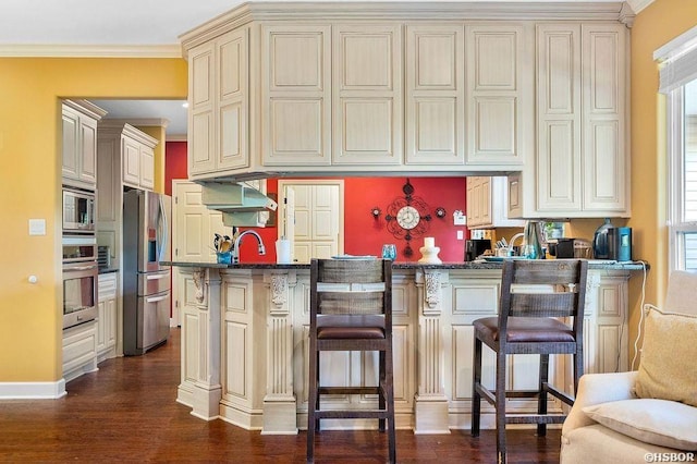 kitchen with a breakfast bar, cream cabinetry, appliances with stainless steel finishes, dark stone countertops, and crown molding