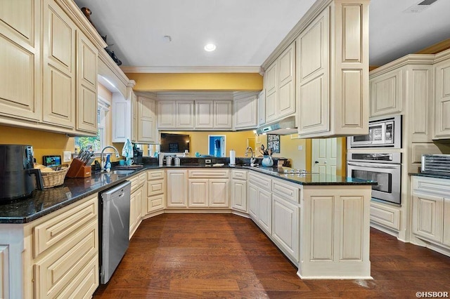 kitchen with cream cabinets, under cabinet range hood, stainless steel appliances, a peninsula, and dark stone counters