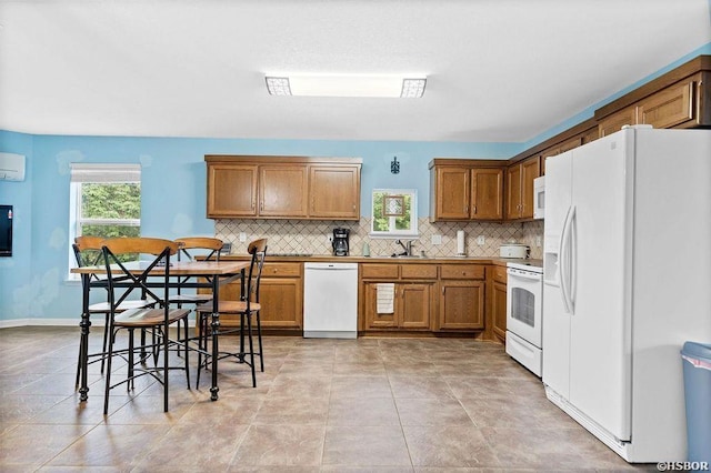 kitchen featuring backsplash, a wall mounted AC, brown cabinetry, a sink, and white appliances