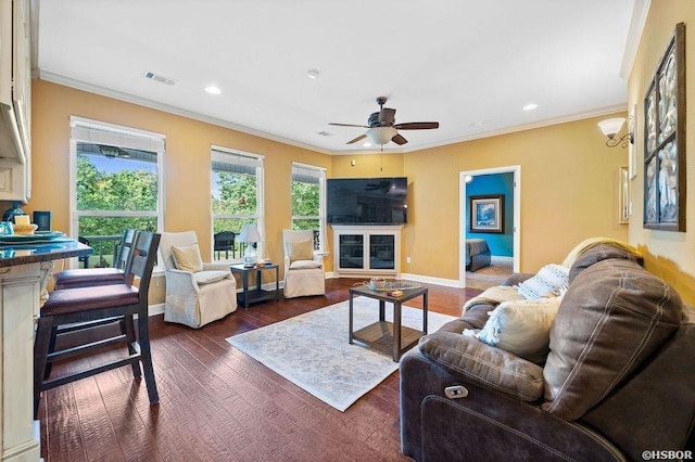 living room with ornamental molding, a glass covered fireplace, dark wood finished floors, and visible vents