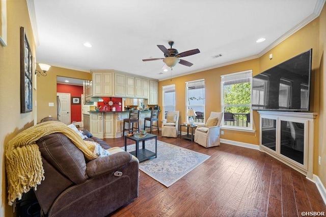 living room with wood finished floors, a ceiling fan, visible vents, baseboards, and ornamental molding