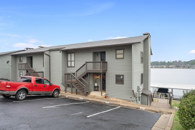 exterior space with stairs, uncovered parking, roof with shingles, and a water view