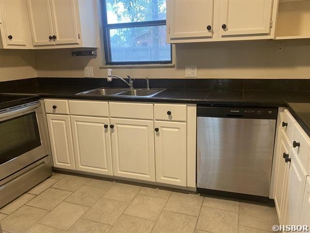 kitchen featuring appliances with stainless steel finishes, dark countertops, a sink, and white cabinetry