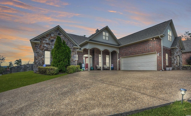 view of front of house with driveway, brick siding, stone siding, fence, and a front yard