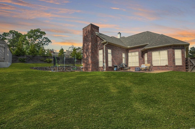 back of property featuring a trampoline, brick siding, a patio, and a lawn