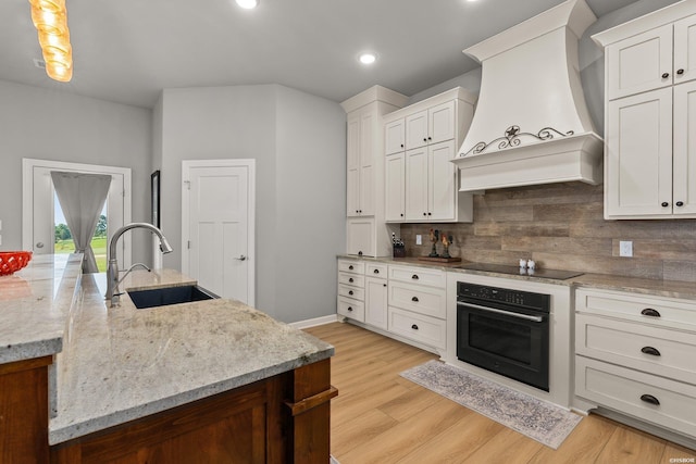 kitchen featuring black appliances, a sink, tasteful backsplash, light wood-style floors, and custom exhaust hood