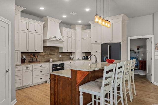 kitchen featuring visible vents, backsplash, custom exhaust hood, white cabinets, and black appliances