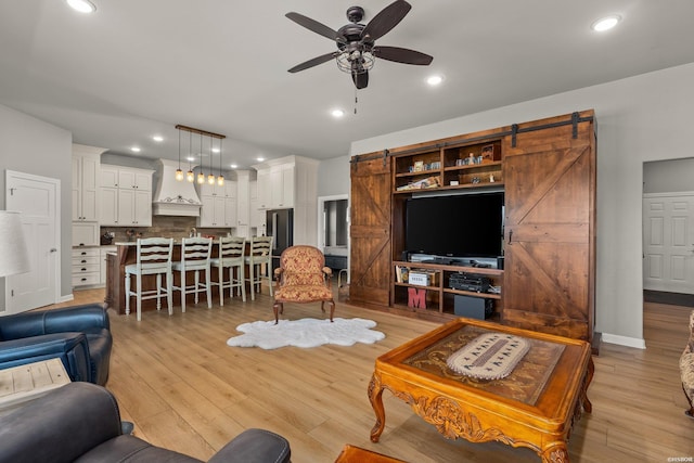 living room featuring light wood finished floors, baseboards, a barn door, recessed lighting, and a ceiling fan