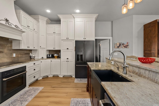 kitchen featuring a sink, hanging light fixtures, black appliances, custom range hood, and white cabinets