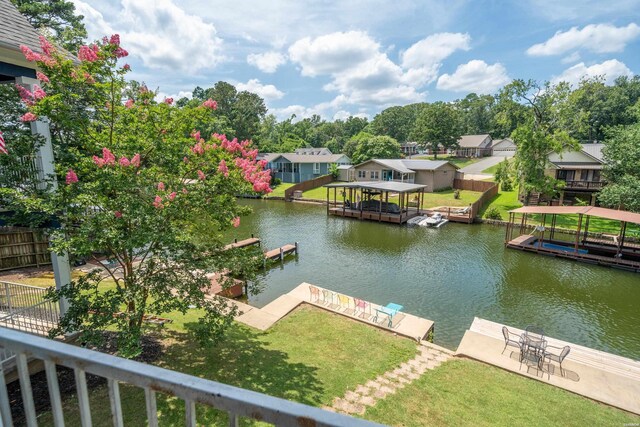 dock area featuring a water view, fence, boat lift, and a lawn