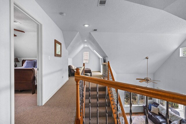 hall with lofted ceiling, carpet floors, visible vents, and an upstairs landing