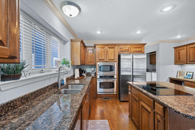 kitchen featuring brown cabinets, crown molding, washing machine and clothes dryer, stainless steel appliances, and a sink