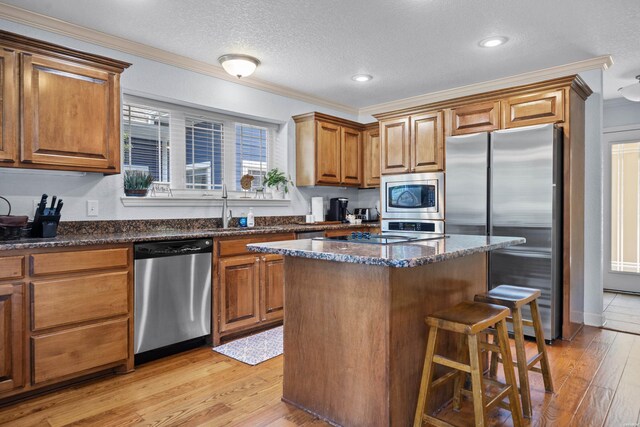 kitchen featuring stainless steel appliances, a kitchen island, light wood-type flooring, brown cabinets, and dark stone countertops