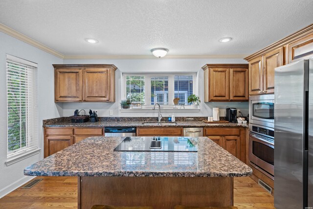 kitchen with appliances with stainless steel finishes, a sink, light wood-style flooring, and a kitchen island