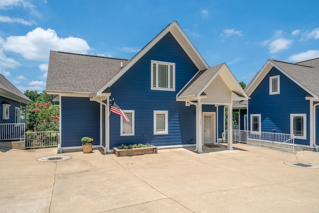 view of front of house featuring a shingled roof, a patio area, and fence