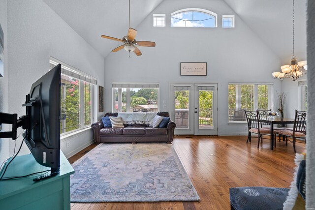 living room with ceiling fan with notable chandelier, high vaulted ceiling, wood finished floors, and baseboards