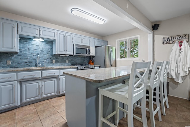 kitchen featuring appliances with stainless steel finishes, a sink, decorative backsplash, a breakfast bar, and light stone counters