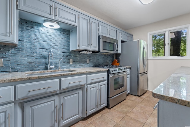 kitchen with appliances with stainless steel finishes, a sink, gray cabinetry, and backsplash