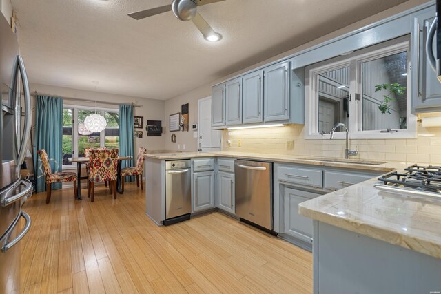kitchen featuring a sink, appliances with stainless steel finishes, gray cabinets, a ceiling fan, and tasteful backsplash