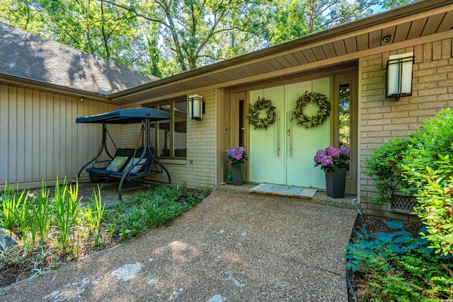 entrance to property featuring brick siding and a shingled roof