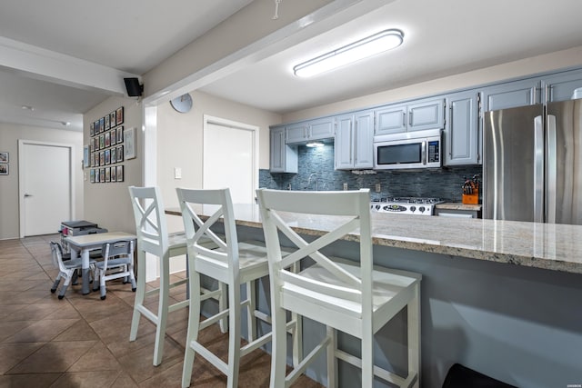 kitchen featuring appliances with stainless steel finishes, tasteful backsplash, a breakfast bar, beam ceiling, and light stone countertops
