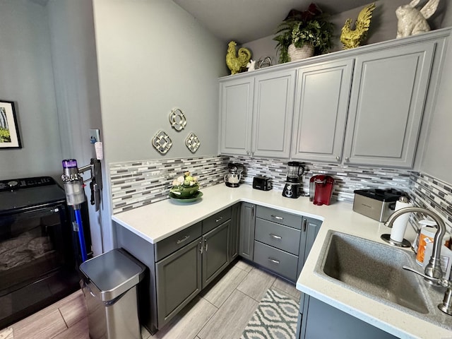 kitchen with tasteful backsplash, light countertops, a sink, and gray cabinetry