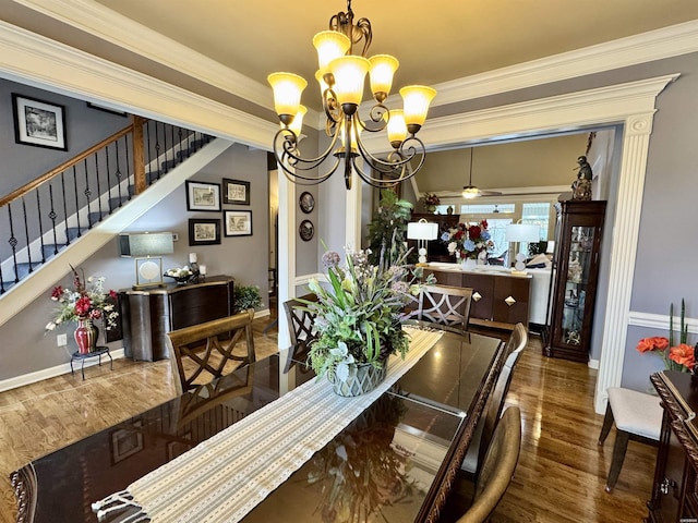 dining area featuring stairs, dark wood-type flooring, ceiling fan with notable chandelier, and crown molding