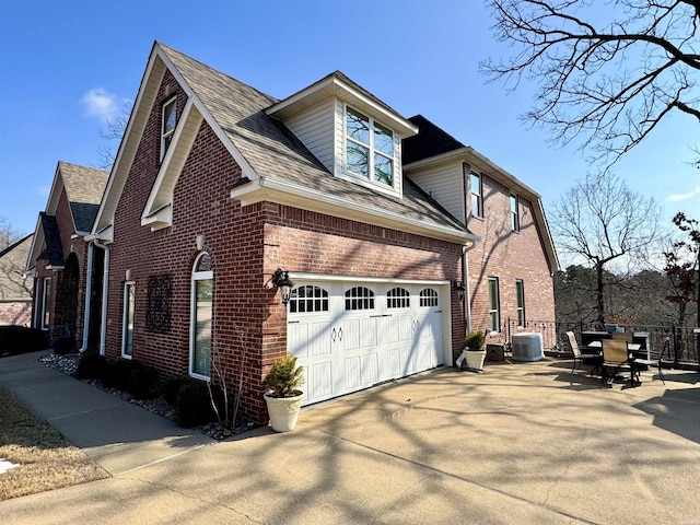 view of side of property featuring brick siding, a shingled roof, concrete driveway, central AC unit, and a garage