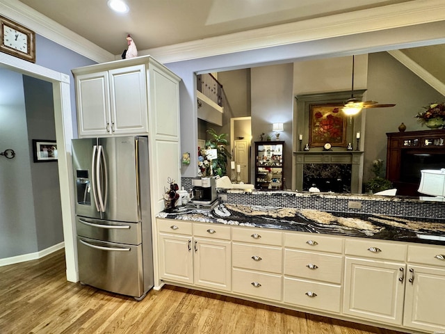 kitchen with light wood-style floors, stainless steel fridge, ornamental molding, and dark stone counters