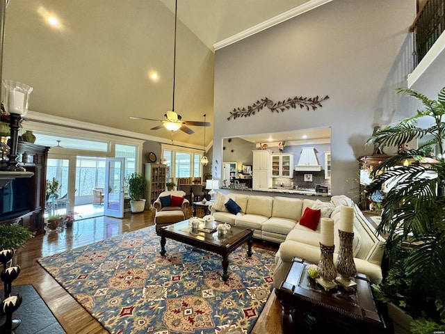 living room featuring dark wood-type flooring, crown molding, ceiling fan, and a high ceiling