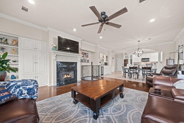 living area with a fireplace, visible vents, wood finished floors, and ornamental molding