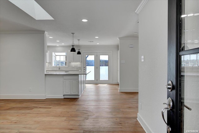 kitchen with ornamental molding, light wood-type flooring, white cabinetry, and tasteful backsplash