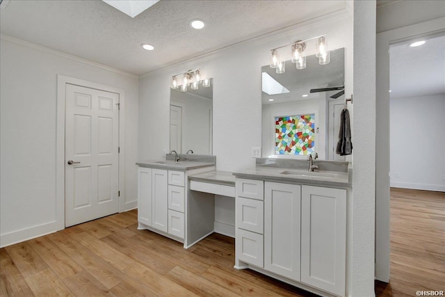 full bathroom with wood finished floors, two vanities, a skylight, and a sink