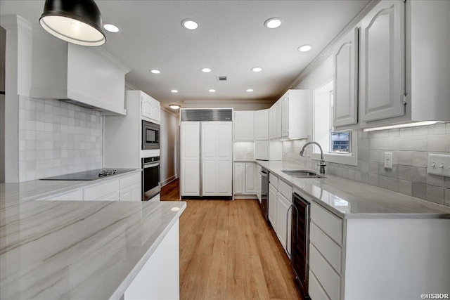 kitchen featuring built in appliances, a sink, white cabinetry, and light stone countertops