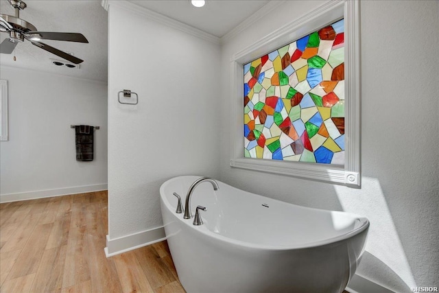 full bath with ceiling fan, a freestanding tub, wood finished floors, baseboards, and crown molding