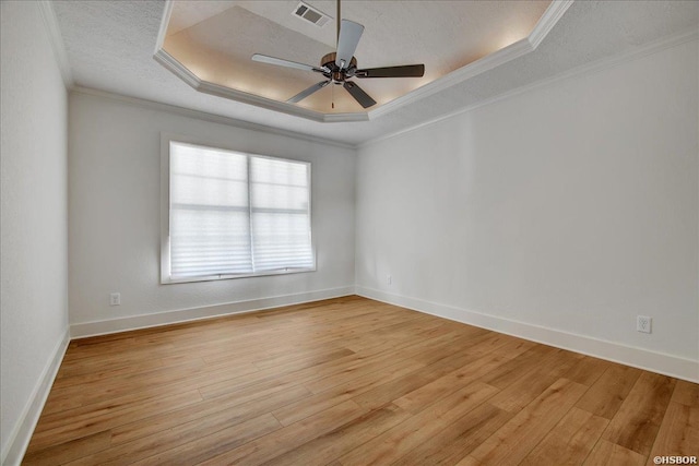 spare room featuring a textured ceiling, a tray ceiling, light wood-type flooring, and crown molding