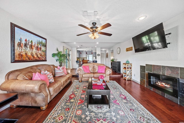 living room with a textured ceiling, visible vents, dark wood finished floors, and a tiled fireplace