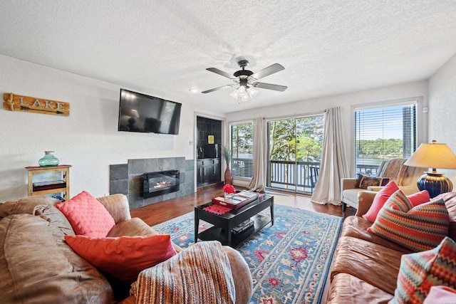 living area with a ceiling fan, a tile fireplace, a textured ceiling, and wood finished floors