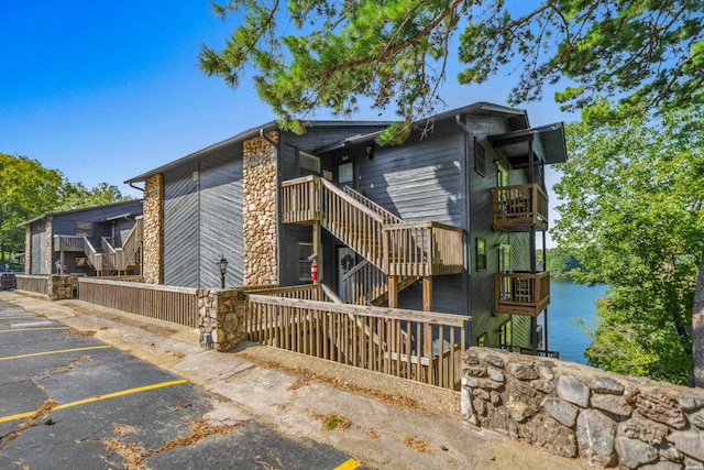 view of property exterior with uncovered parking, a water view, and stairway