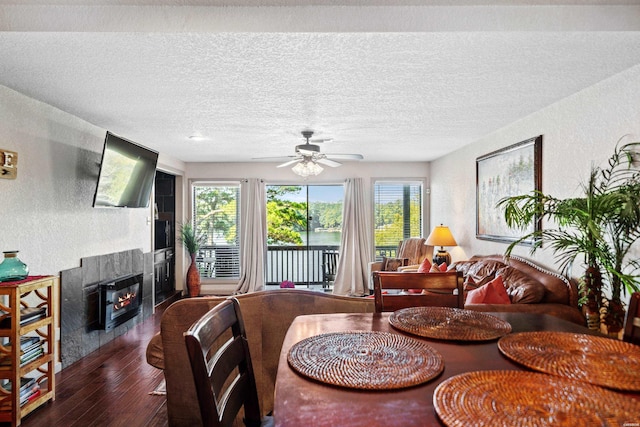 dining space with a textured ceiling, a textured wall, ceiling fan, dark wood-style flooring, and a glass covered fireplace