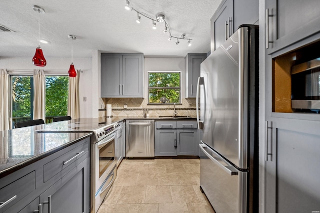 kitchen with stainless steel appliances, a sink, hanging light fixtures, and gray cabinetry