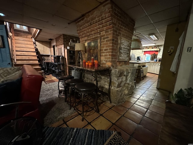 interior space with tile patterned flooring, a drop ceiling, stairway, and brick wall