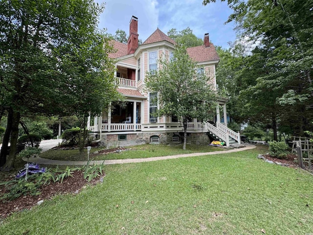 back of property featuring a shingled roof, a chimney, a lawn, and a balcony