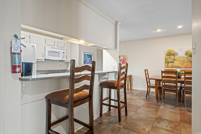 5371 Central Ave Unit 6J, Hot Springs, AR 71913 - kitchen with white appliances, a kitchen breakfast bar, a textured ceiling, crown molding, and white cabinetry
