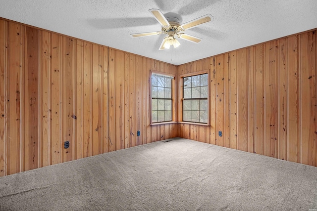 spare room featuring wood walls, carpet, ceiling fan, and a textured ceiling