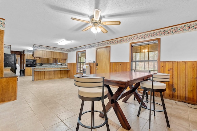 dining room featuring light tile patterned floors, a ceiling fan, wainscoting, a textured ceiling, and wood walls